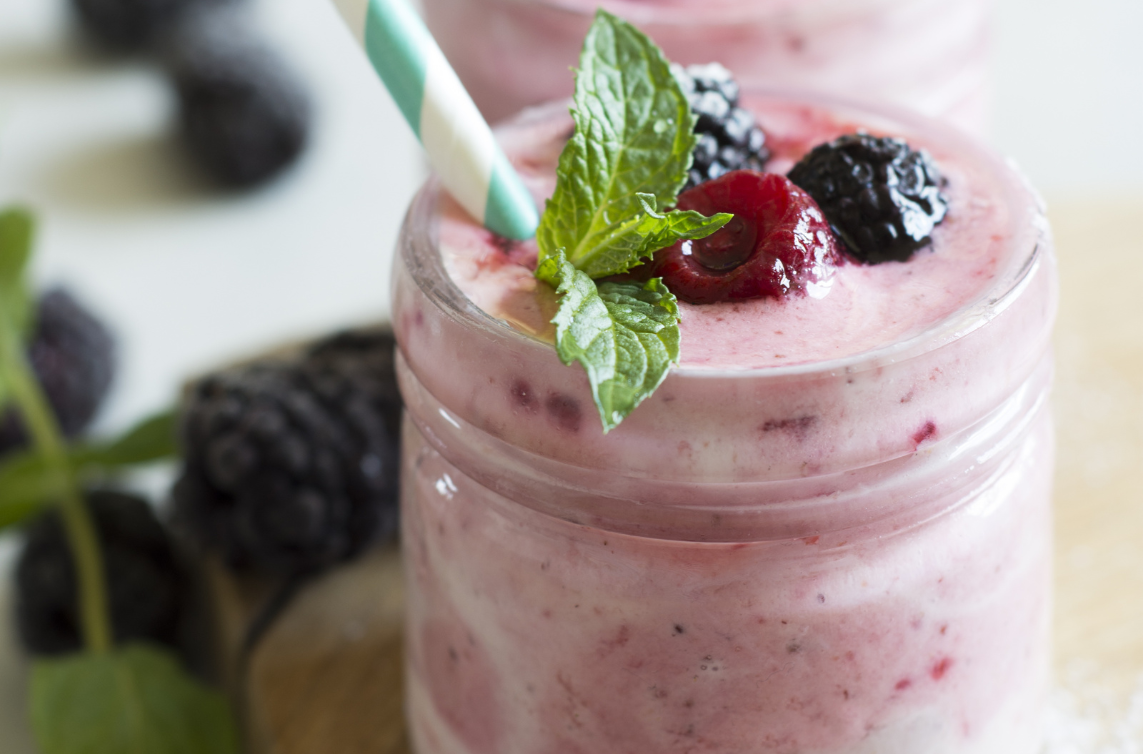smoothie in small glass with berries on top and straws