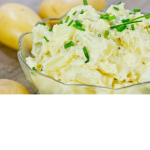 bowl of potato salad with a few potatoes beside bowl